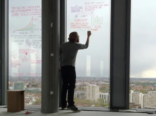 Person writing notes and diagrams on a window with city view by Alexander Roncaldier