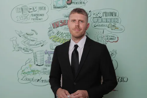 Man in black suit in front of illustrated wall background by Alexander Roncaldier