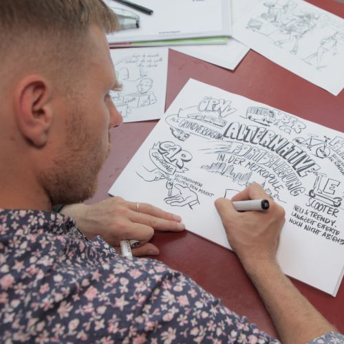 Artist Alexander Roncaldier drawing sketches on paper at a red table