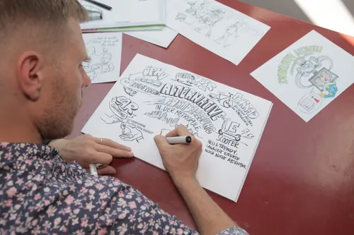 Artist Alexander Roncaldier drawing sketches on paper at a red table
