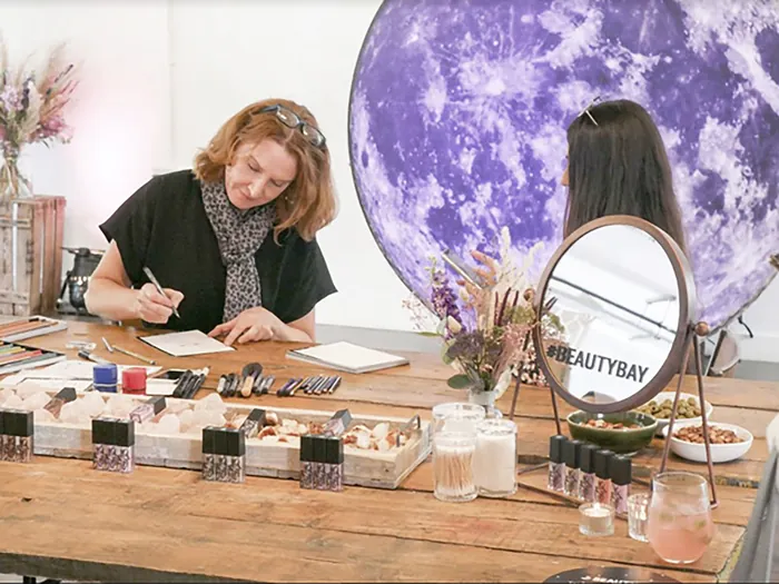 Live illustrator drawing at table with moon backdrop and makeup display