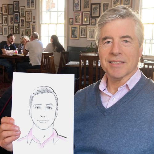 Man holding a live portrait drawing of himself in a cafe