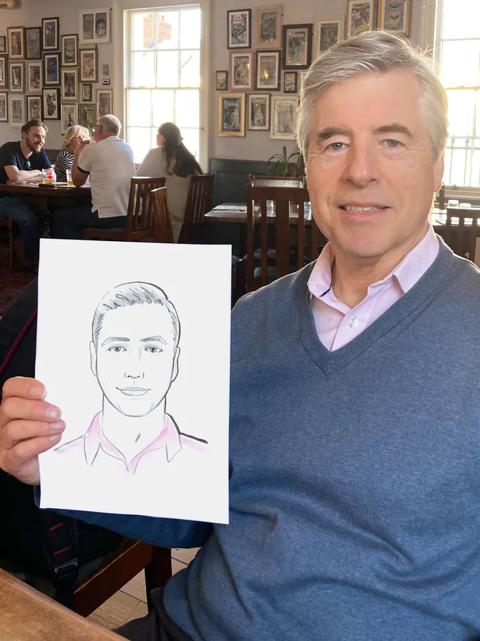 Man holding a live portrait drawing of himself in a cafe