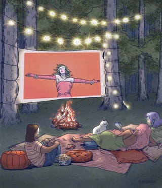 Friends enjoying outdoor movie night by campfire with string lights in forest