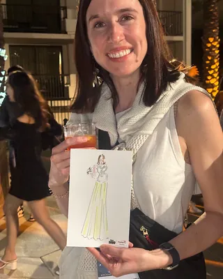Smiling woman holding a fashion illustration at an outdoor event