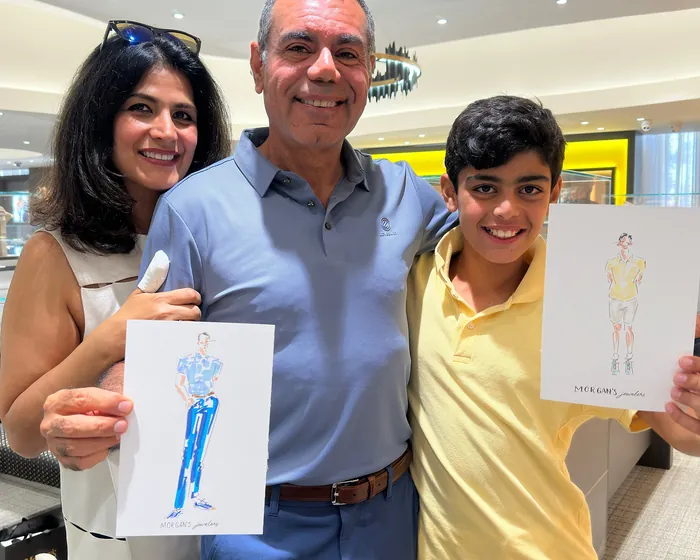 Three people smiling and holding fashion sketches in a mall