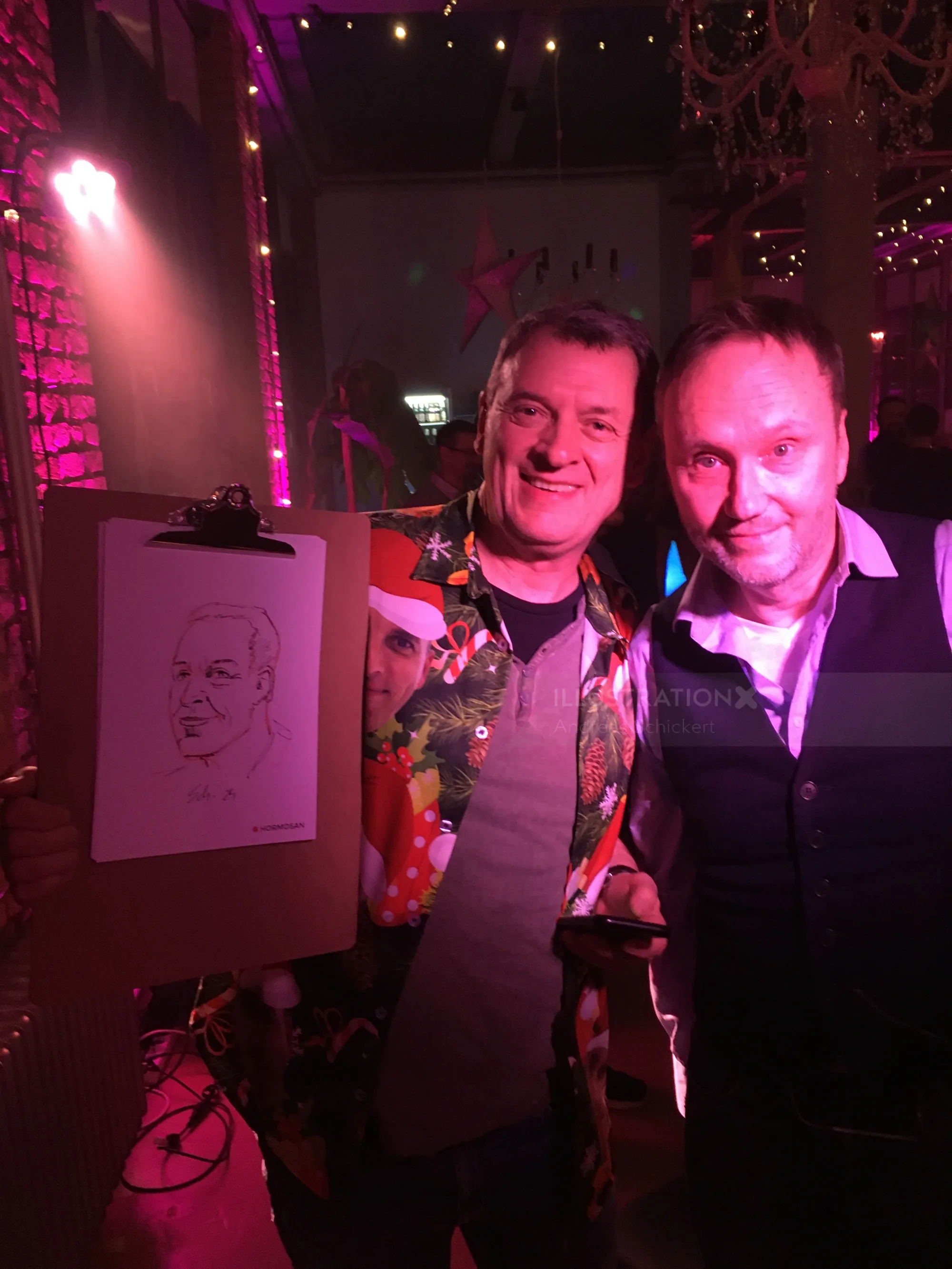 Two men smiling next to a caricature drawing in a dimly lit party setting.