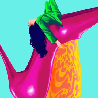 Woman in green jacket leaning on giant pink stiletto shoe against blue background