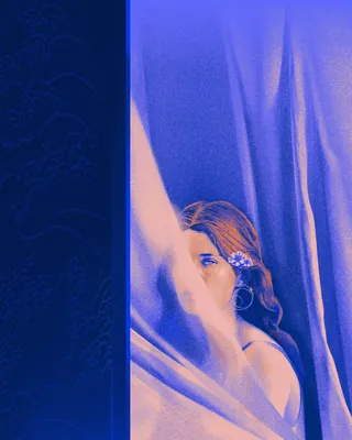 Woman peeking from behind a blue curtain in artistic lighting