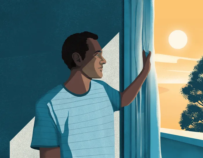 Man gazing out window at sunrise with hand on curtain