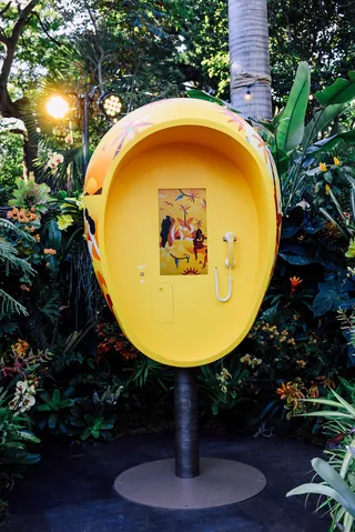 Yellow ear-shaped phone booth in lush green garden
