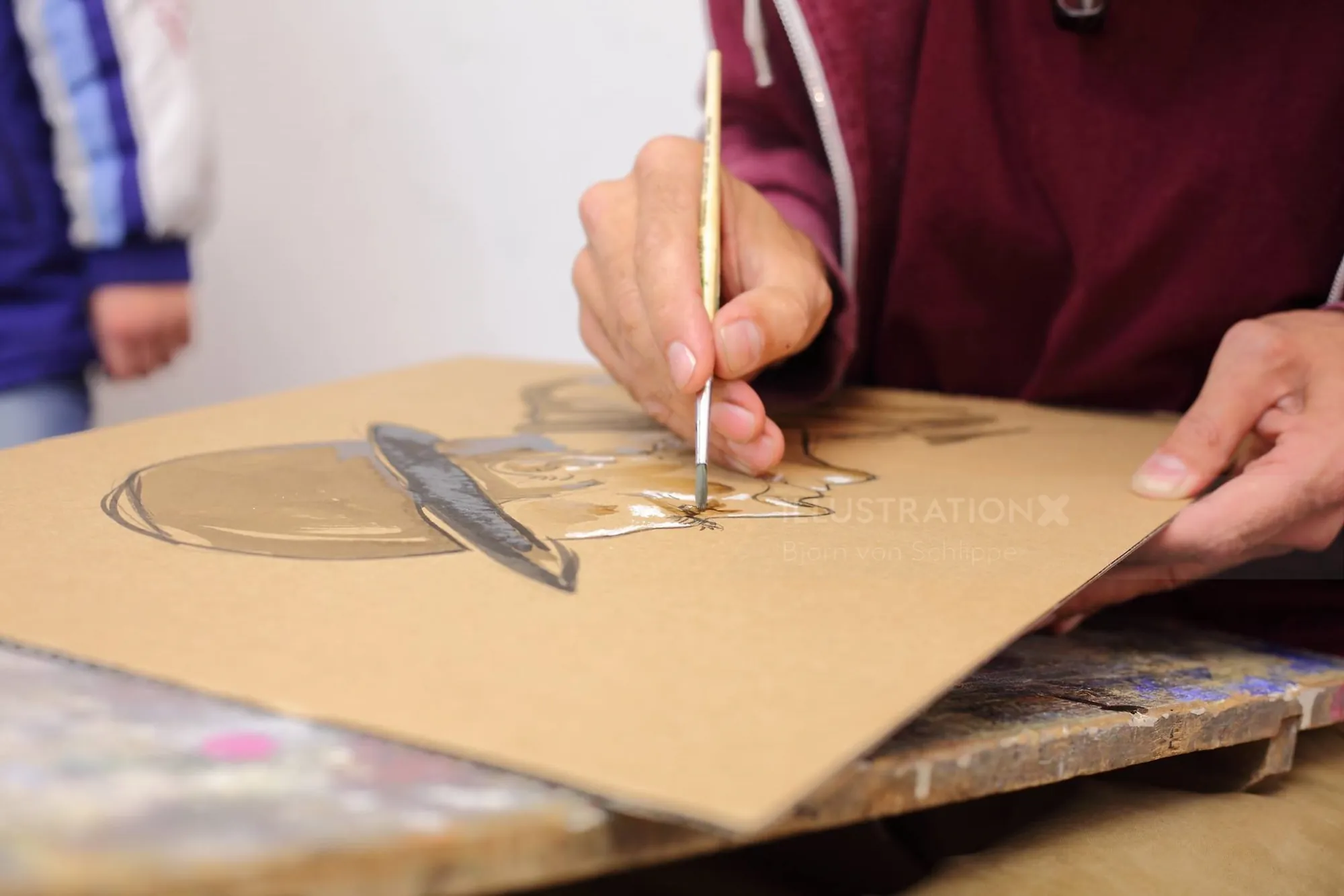 Hands drawing on brown cardboard with paintbrush and pencil by Björn von Schlippe
