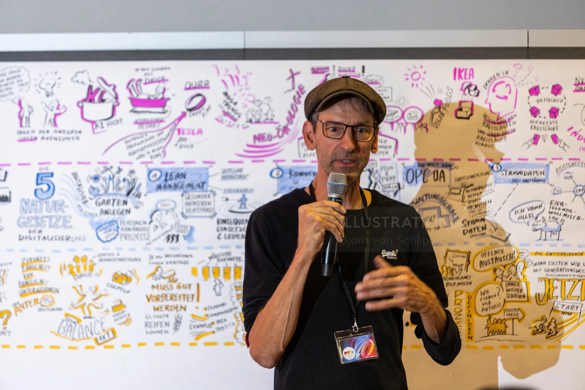 Man speaking with microphone in front of whiteboard with notes and diagrams