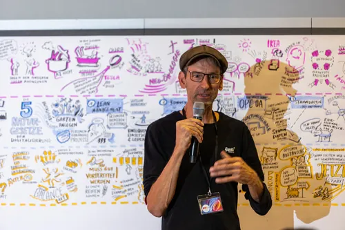 Man speaking with microphone in front of whiteboard with notes and diagrams