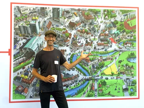 Man standing next to large colorful illustrated town map.