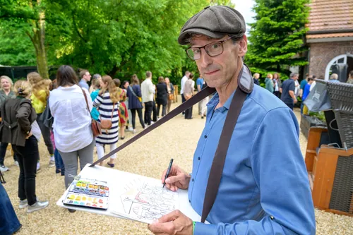 Male artist sketching outdoors with people gathered behind him