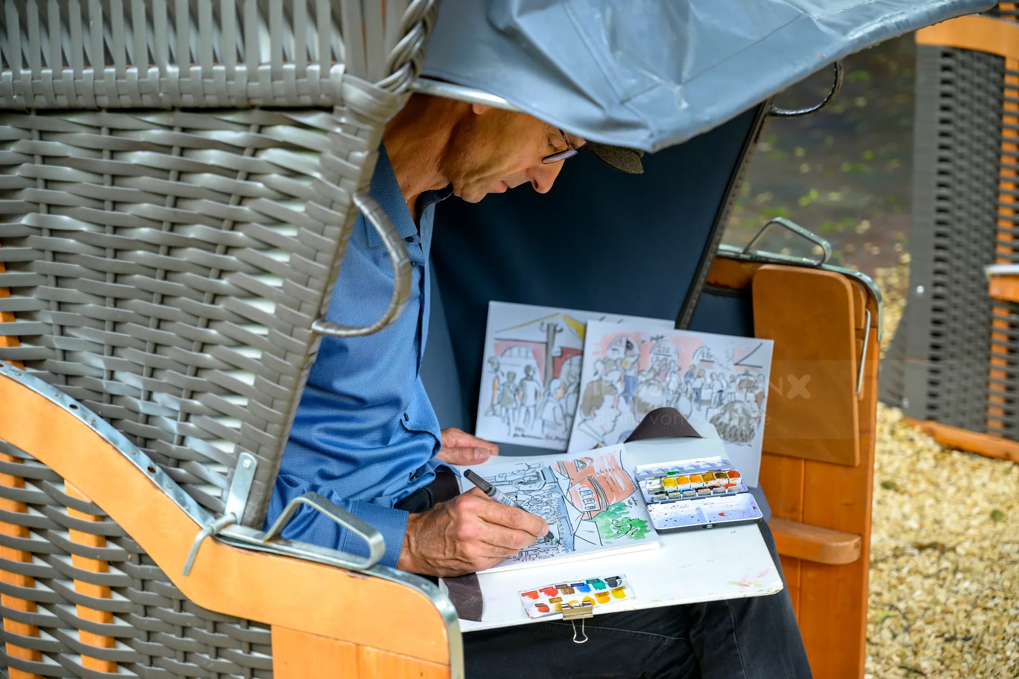 Artist drawing colorful sketches sitting outdoor in a wicker chair with canopy