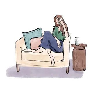 Woman sitting on couch wiping her face with tissue, glass of water nearby by Briana Kranz