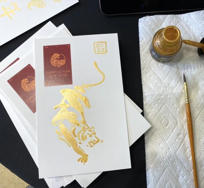 White cards with gold foil tiger design and brush with paint jar by Briana Kranz