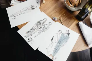 Three detailed fashion sketches on paper on a wooden table by Briana Kranz Live Event Drawing