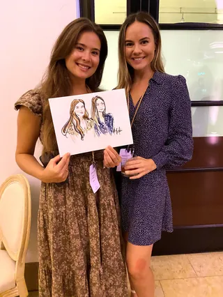 Two women smiling holding a portrait sketch between them