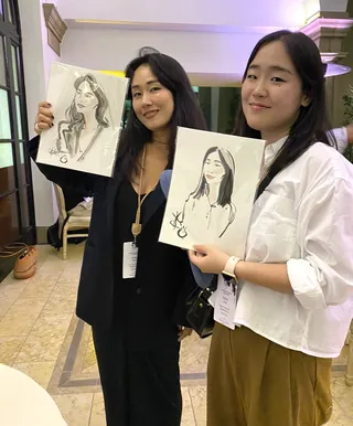 Two women holding portrait sketches indoors smiling