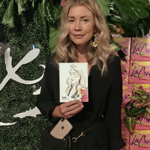 Woman with blonde hair holding a portrait sketch in a garden setting