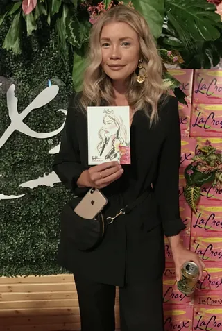 Woman with blonde hair holding a portrait sketch in a garden setting