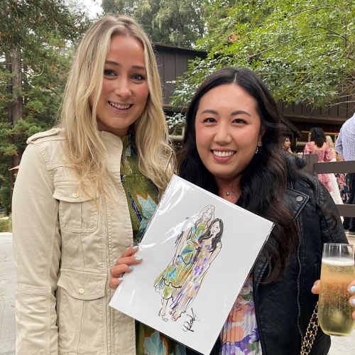 Two women outdoors, one holding an art print, both smiling.