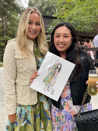 Two women outdoors, one holding an art print, both smiling.