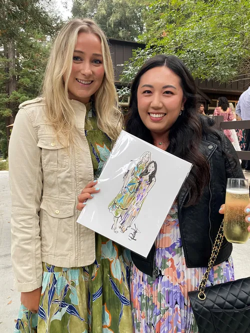 Two women outdoors, one holding an art print, both smiling.