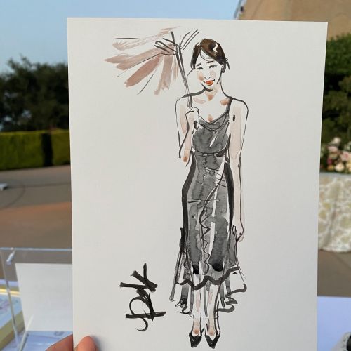 Hand holding a quick ink and watercolor portrait of a woman in a dress