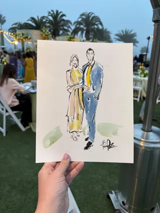 Hand holding fashion sketch of a couple at outdoor event