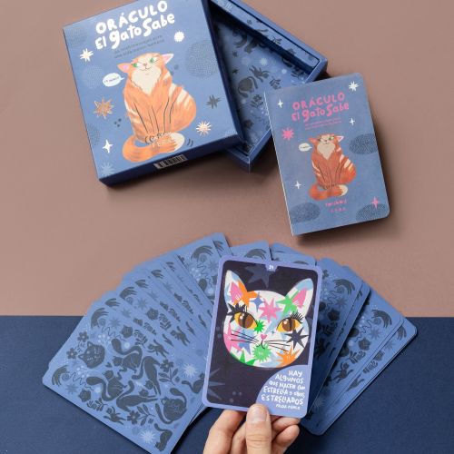 Hand holding a colorful cat oracle card over a deck and box
