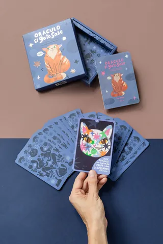 Hand holding a colorful cat oracle card over a deck and box