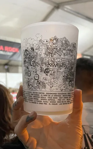 Hand holding transparent cup with detailed black and white doodles and text.