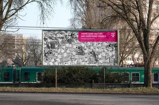 Billboard with German text above green train and bare trees outdoors