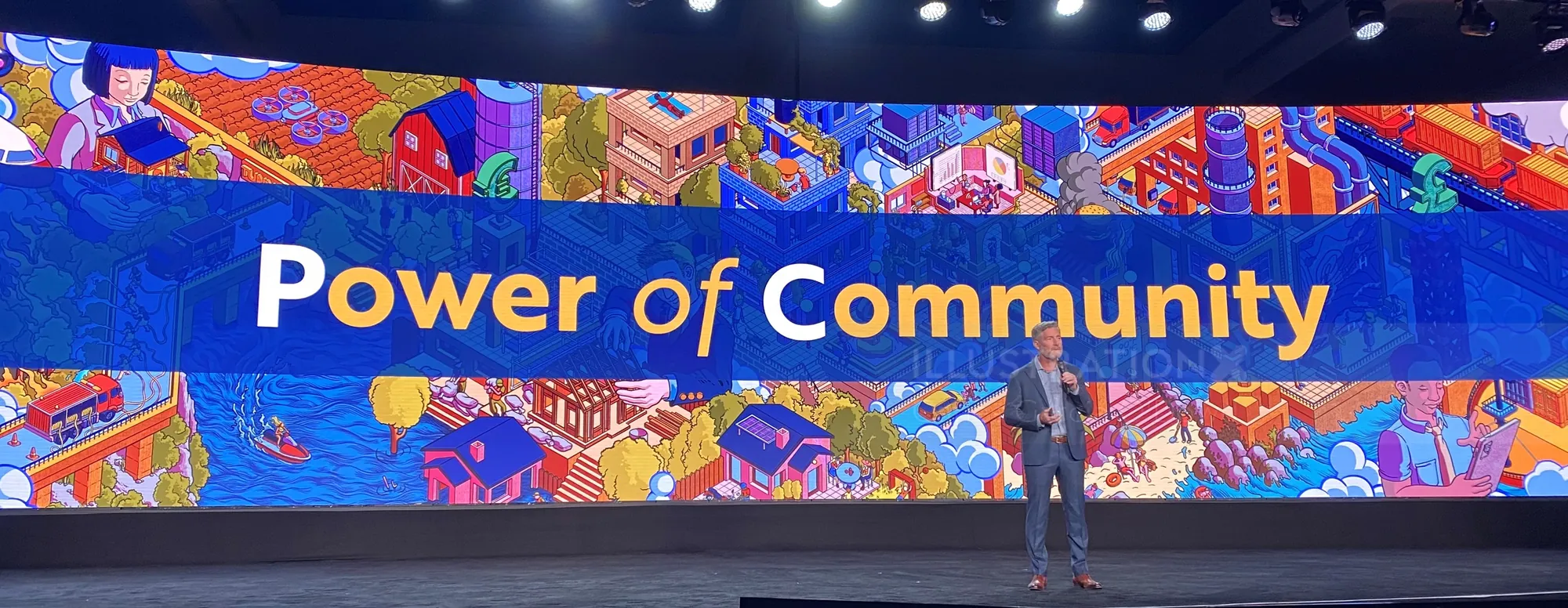 Person speaking on stage with Power of Community banner behind