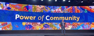 Person speaking on stage with Power of Community banner behind