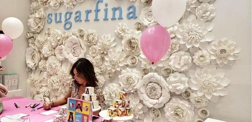Caroline So drawing at Sugarfina store with floral wall and pink balloons