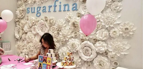 Caroline So drawing at Sugarfina store with floral wall and pink balloons