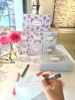 Fresh branded boxes stacked with pink roses and a hand writing on a box by Caroline So