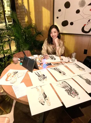 Woman showing fashion sketches laid out on a round table in a warm room