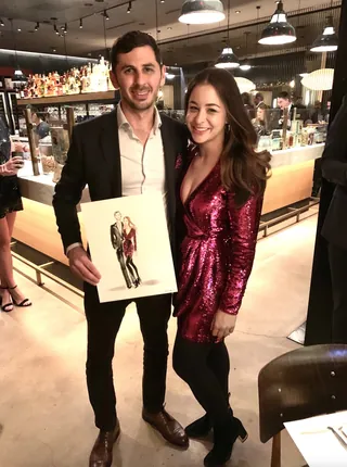 Man and woman in formal attire holding a fashion sketch at a party