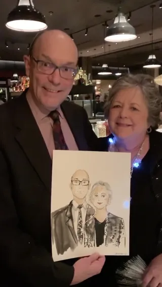 Man and woman holding a portrait sketch in a restaurant setting.