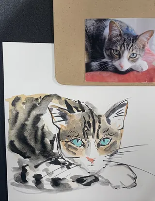 Watercolor painting of a tabby cat with blue eyes beside a photo