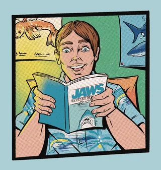 Person reading a book titled JAWS with shark posters behind