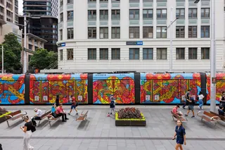 Brightly painted tram in city plaza with people walking nearby