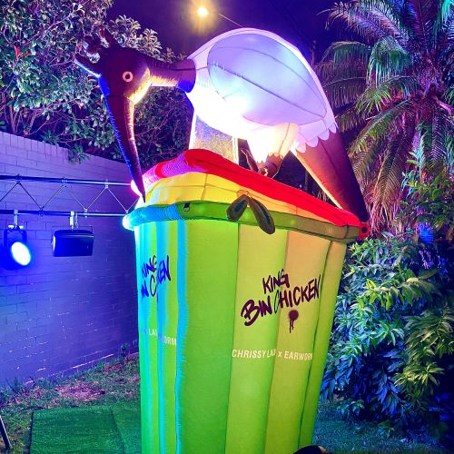Brightly lit bird sculpture on green trash bin outdoors at night