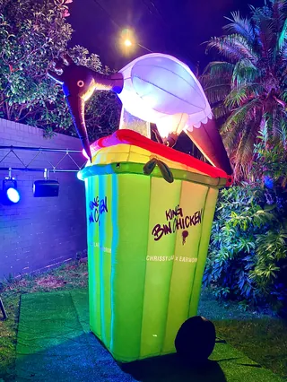 Brightly lit bird sculpture on green trash bin outdoors at night